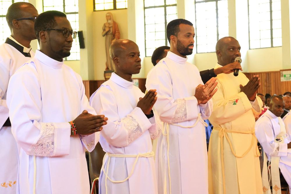 Deacon Justus Nyabuga Barongo speaking at the microphone with fellow religious