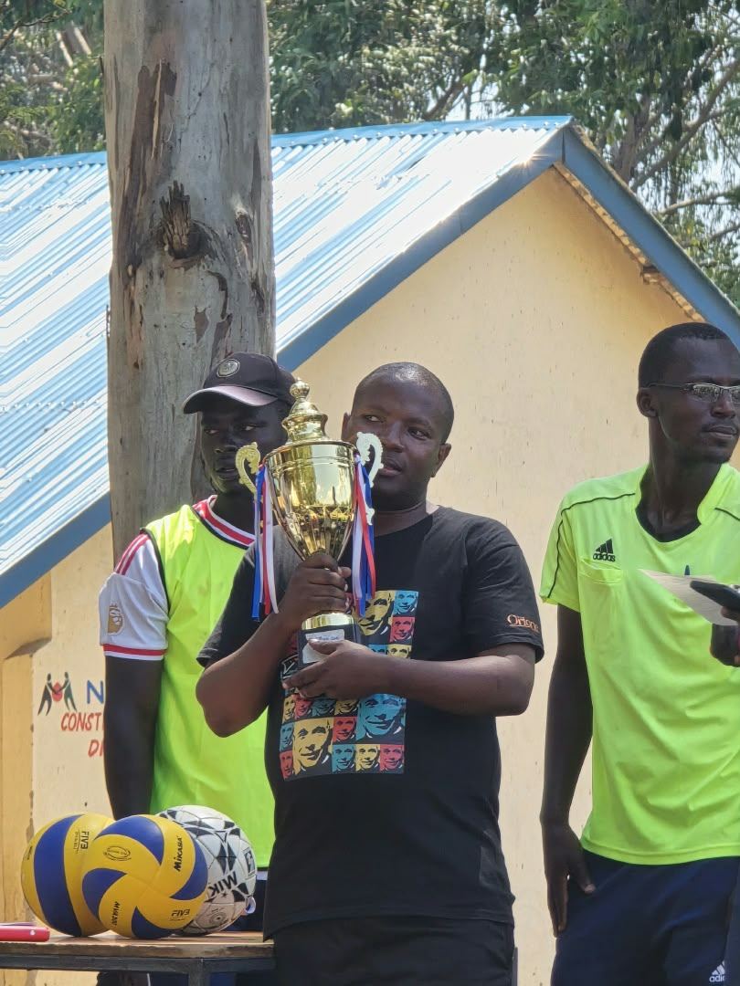 A guest holding the trophy beside the volleyball and football for the tournament